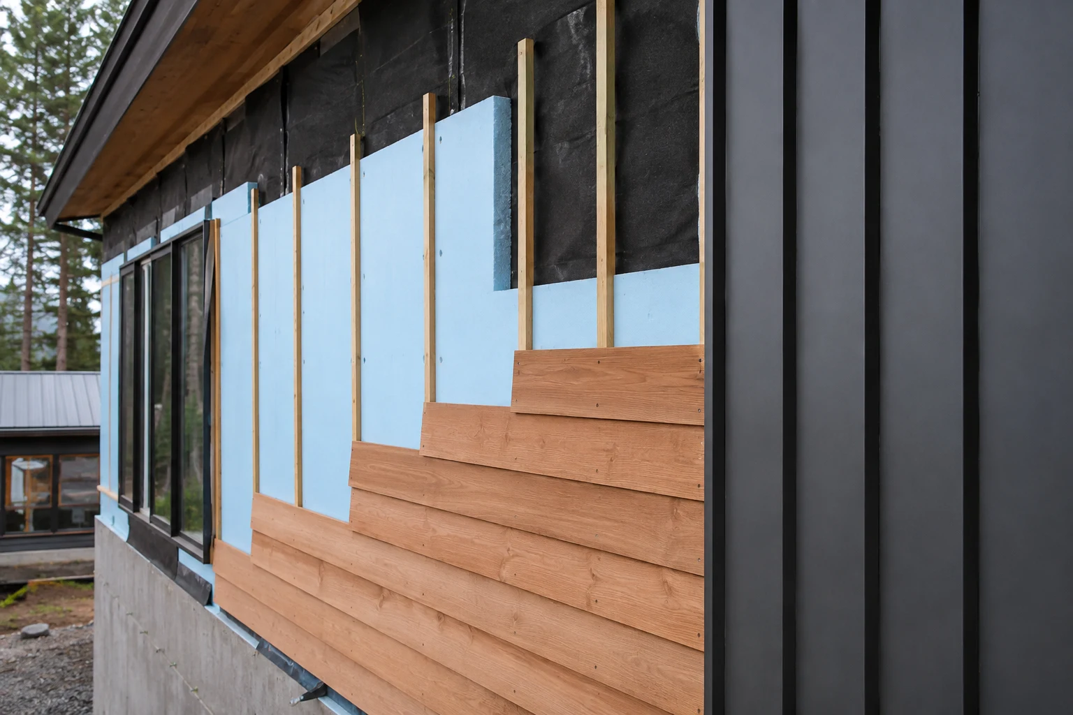 Rainscreen facade installation showing membrane, exterior insulation, vertical furring, wood siding, and panel cladding